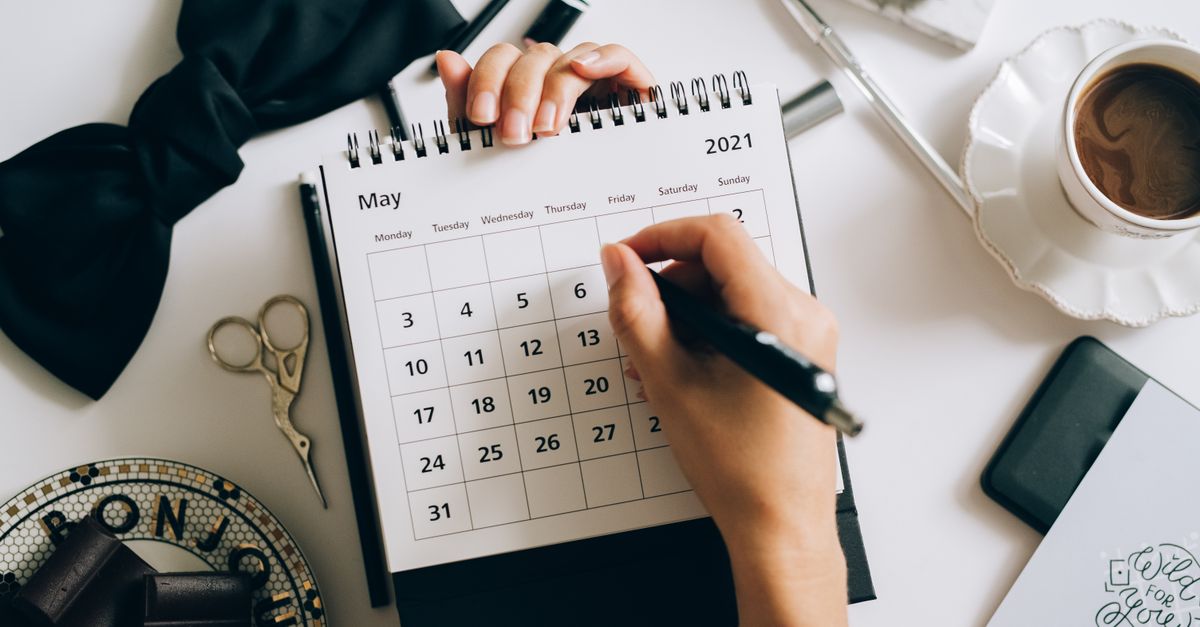 Top view of hands using a planner with coffee and accessories, focused on May 2021 calendar.